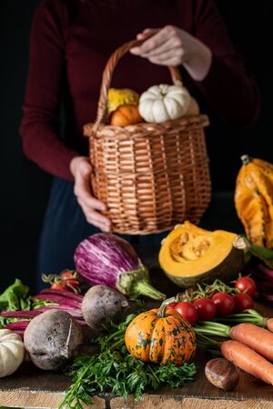 Dark still life, female hands holding wicker basket with organic vegetables assortmentの写真素材