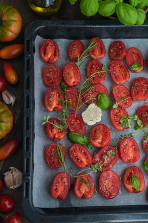 Italian cuisine, tomatoes on baking sheet with aromatic herbs, thyme, basic, garlic, olive oil, top viewの写真素材