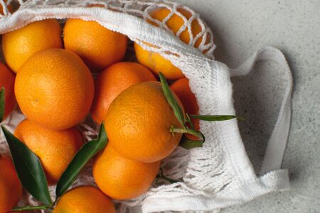 Eco christmas concept, organic ripe clementines in cotton mesh bag, light gray background, copy space, top viewの写真素材