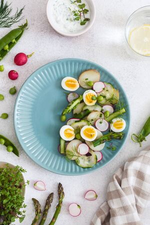 Healthy fresh detox vegetarian vegetable salad, top view on light background. Asparagus, radish, green peas, potato, cucumber, microgreensの写真素材