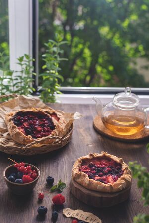 Summer homemade pastry, galette with berries on rustic wooden background with herbal teaの写真素材