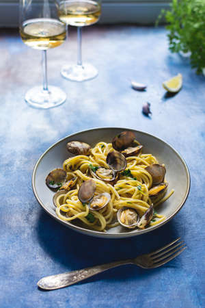 Italian cuisine, spaghetti pasta with vongole clams on blue background, glass of white wineの写真素材