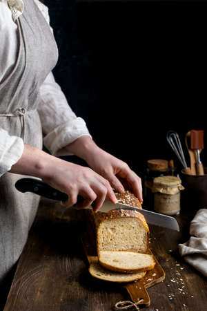 Close up of female hands cutting homemade whole grain sourdough bread on dark background, copy spaceの写真素材