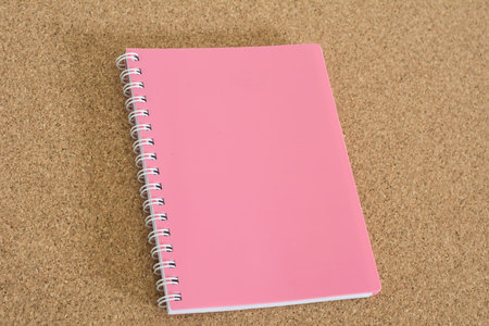 Blank spiral notebook pink on cork board background.
