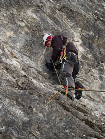 Male climber ascending vertical cliff face. Winter