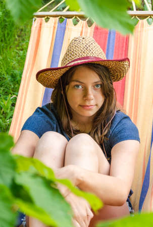 portrait of a cute girl in a straw hat lying in a hammock, a cute young cowgirl, relaxing in the summer garden in a hammock.の写真素材