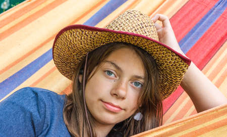 portrait of a cute girl in a straw hat lying in a hammock, a cute young cowgirl, relaxing in the summer garden in a hammock.の写真素材