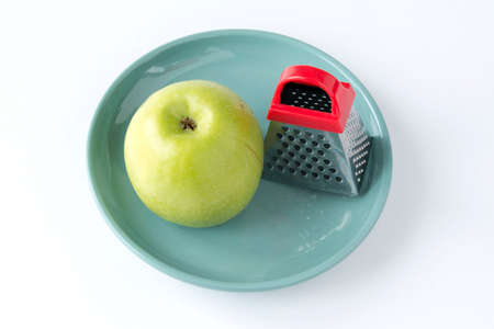 Juicy ripe green apple and a small grater on a turquoise plate, isolated on a white backgroundの写真素材