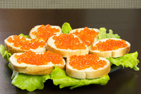 delicious sandwich with red caviar, butter and fresh lettuce leaves on a plateの写真素材