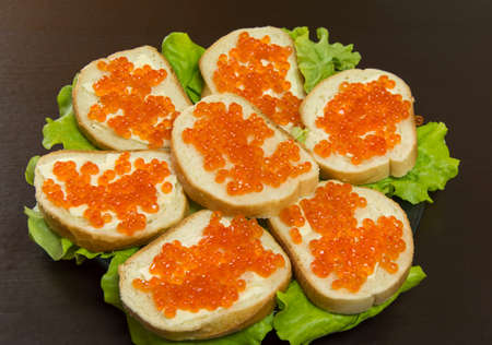 delicious sandwich with red caviar, butter and fresh lettuce leaves on a plateの写真素材