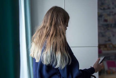 Teenage girl with loose hair with dyed ends stares at smartphone, faces not visibleの写真素材