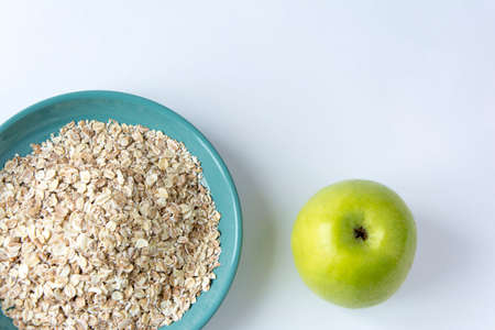 oatmeal flakes in a turquoise plate and a green apple on a white background, healthy breakfast, herculesの写真素材