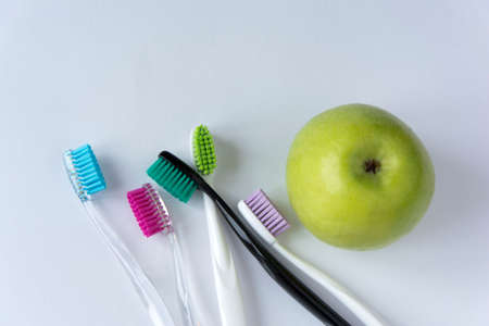 A green juicy strong apple and several colored toothbrushes next to it, on a white backgroundの写真素材