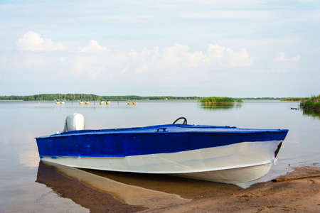 Aluminum blue fishing boat with a motor near the lake shore, fishing, tourism, active recreation, lifestyle. Background of nature. Natural landscape.の写真素材