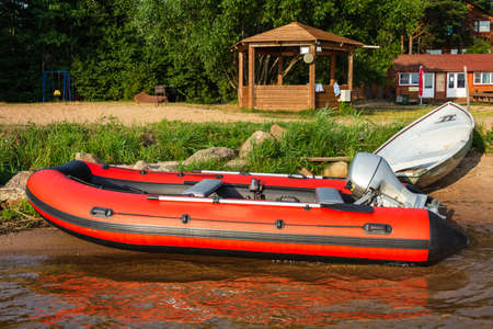 Red inflatable rubber boat with a motor near the lake shore, fishing, tourism, active recreation.の写真素材