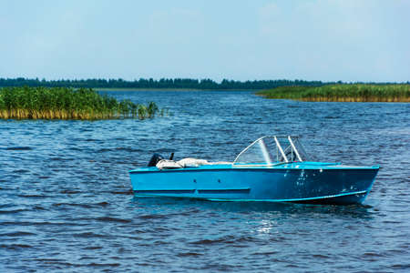 Aluminum blue fishing boat with a motor near the lake shore, fishing, active recreation, Background of nature. Natural landscape.の写真素材