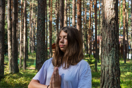 a young pretty girl meditates in nature in the forest among tall pines, illuminated by the sun's rays, a girl meditates, enjoy the tranquility, silence, prayer, tranquilityの写真素材