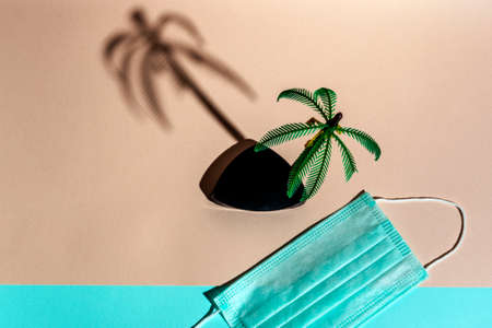 palm tree figurine and medical protective mask on a pink and turquoise background, minimalism, vacation at the sea during the pandemic, vacation during covid 19の写真素材