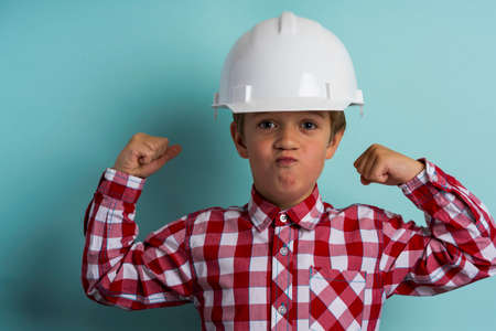 A cute boy in a construction helmet protects his head, A portrait of a small builder in a helmet, his hands are on his head, an engineer, a young architect.の写真素材