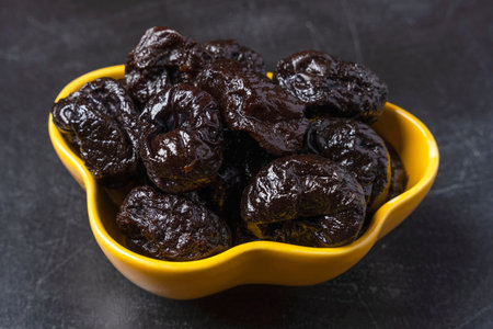 Sweet delicious prunes in a yellow plate on a black background. Delicious natural delicacy, dessert.