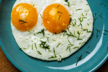 fried eggs on a turquoise plate sprinkled with dill, top view.の写真素材