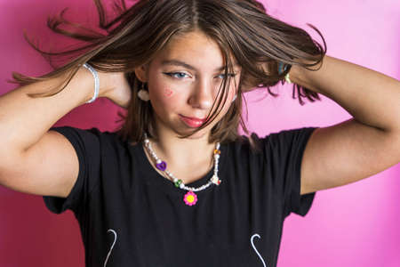Portrait of a beautiful Caucasian girl shaking her hair, posing on a pink background in a black T-shirt, hearts painted on her cheeksの写真素材