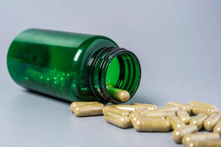Capsules with vitamins and minerals are poured out of the jar on a gray background. Close-up, Health maintenance concept, medication, nutritional supplementsの写真素材