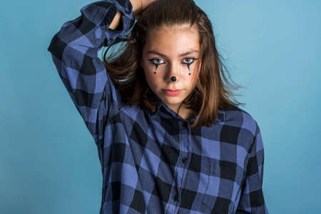 Cute, fashionable, cheeky Caucasian brunette with clown makeup and long hair, dressed in a plaid shirt on a blue background, in the style of a joker, A charming young woman with a face painted like a clown.の写真素材