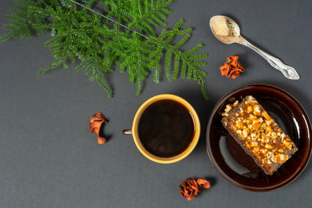 A cup of coffee and a cake on a saucer on a dark background top view, green branch, Space for textの写真素材