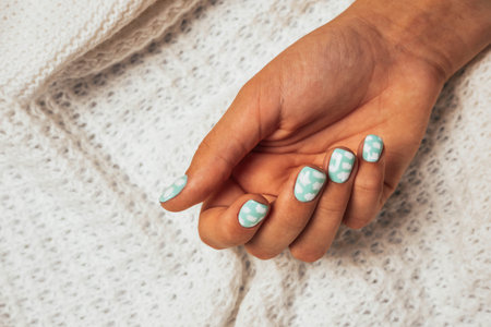 A beautiful female hand with a colored manicure on the background of a woolen white knitted plaid