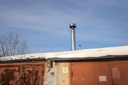 Metal chimney of a garage stove above the roofs of garage boxesの写真素材