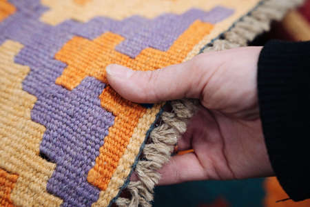 a womans hand selects and touches a colored carpet in a storeの写真素材
