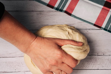 The chefs hands prepare and knead fresh homemade pizza dough on the kitchen table