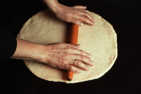 The chefs hands roll out fresh homemade pizza dough on the kitchen table with a rolling pin