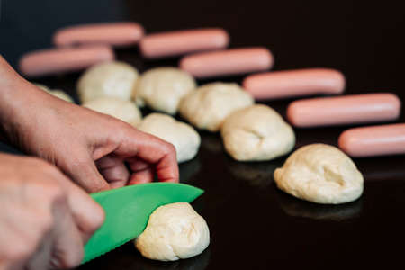 Womens hands cut off a piece of dough with a plastic cooking knife for cooking sausages in doughの写真素材