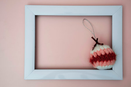 knitted, soft, handmade colored Christmas ball and an empty photo frame on a light peach background