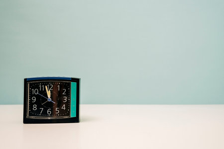 square modern alarm clock on the table on a turquoise background, time 23:55, 11:55