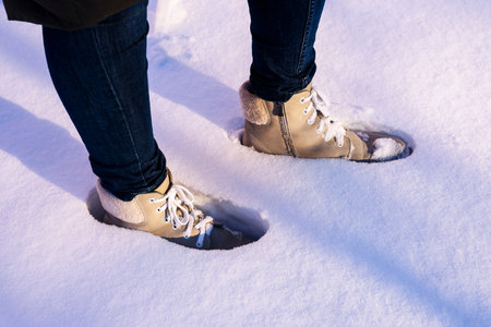 womens feet in light suede boots and blue jeans are standing in the snow