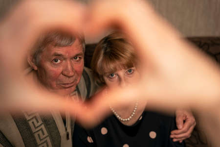 A cute older man hugs a cute older woman, a view through the heart from his handsの写真素材