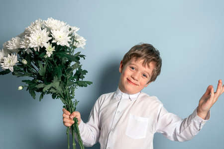 A cute Caucasian boy in a white shirt holds a bouquet of white flowers in his hand and smiles.の写真素材