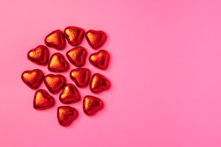 Bright Festive Pink background with shiny candies in the shape of hearts wrapped in foil