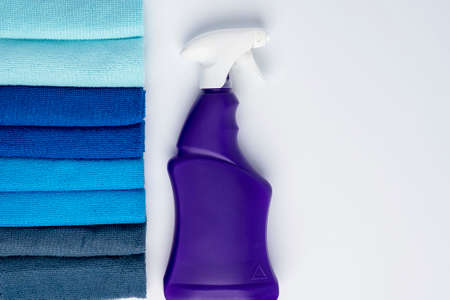 A purple bottle of cleanser with a spray and colored cleaning cloths on a white backgroundの写真素材