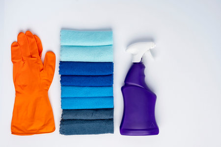 A purple bottle of cleanser with a spray and colored cleaning cloths on a white background