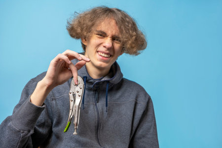 fixing pliers pinched the finger of a teenager with wavy hair dressed in a gray hoodie