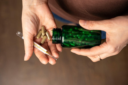 womens hands hold a medical thermometer and tablets, capsules. healthcare conceptの写真素材