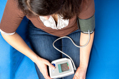 a middle-aged Caucasian woman measures blood pressure sitting on a couch, top view