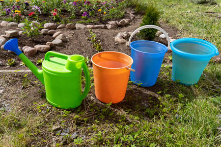 colored buckets for watering flowers in flower bed and a watering canの写真素材