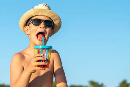 boy in a hat and sunglasses drinks juice through a straw on the beachの写真素材