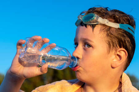 happy boy in swimming glasses drinks water from a bottle on the beachの写真素材