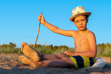 boy in a sun hat and swimming shorts is relaxing sitting on the beachの写真素材